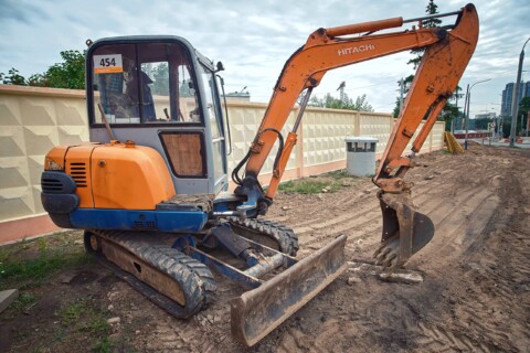 Zdjęcie przedstawiające małą koparkę marki Hitachi zaparkowaną na placu budowy.