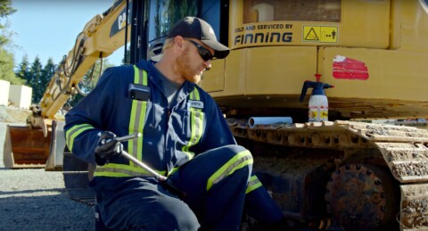 Mechanik w odzieży roboczej z narzędziem w ręku, naprawiający maszynę budowlaną marki CAT.