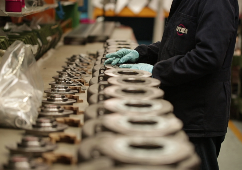 Pracownik w ciemnym kombinezonie i rękawiczkach układa metalowe części.