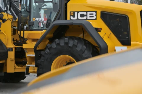 Zbliżenie na koparkę JCB w kolorze żółtym, widok na koło i kabinę operatora