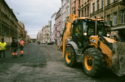 Koparko-ładowarka JCB 3CX pracująca przy remoncie ulicy w centrum miasta, z widocznymi robotami drogowymi i zabudową kamieniczną
