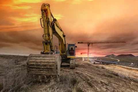 Koparka gąsienicowa wykonująca prace ziemne na otwartym terenie o zachodzie słońca