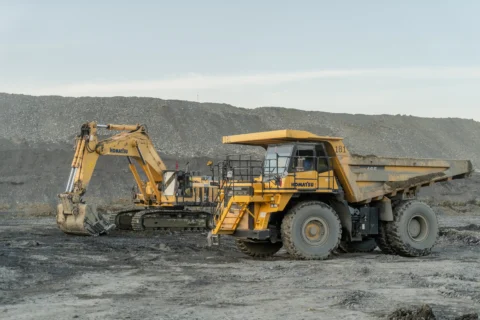 Duże wozidło technologiczne oraz koparka gąsienicowa pracujące na terenie kopalni odkrywkowej