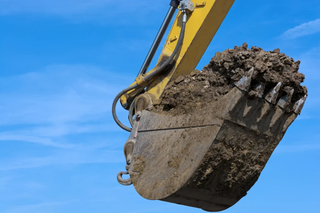 łyżka do minikoparki podczas kopania ziemi na tle nieba